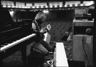 Trimpin, kneeling next to piano, looking right, holding computer part, Telluride CO., (1989)