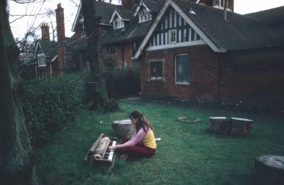 Annea Lockwood sitting in her backyard, playing a piano keyboard on the grass, Ingatestone (1972)