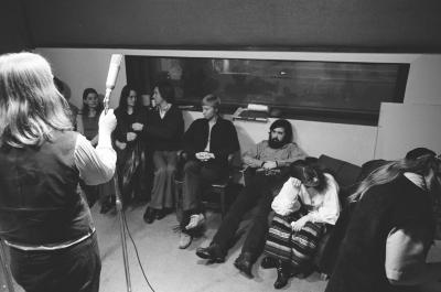 A group of people sitting in the KPFA studio while staff set up microphones, vs. 2, (1972)