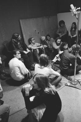 A group of people sitting in the KPFA studio waiting to participate in a performance of Annea Lockwood's "Music for Multiple Hummers", vs. 2 (1972)