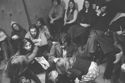A group of people sitting in the KPFA studio waiting to participate in a performance of Annea Lockwood's "Music for Multiple Hummers" (1972)