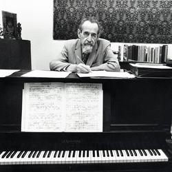 Dane Rudhyar, head a shoulders portrait, facing forward, standing behind piano with musical score displayed (retouched)