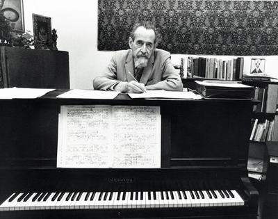 Dane Rudhyar, head a shoulders portrait, facing forward, standing behind piano with musical score displayed (retouched)