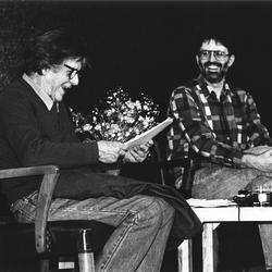 John Cage & Charles Amirkhanian (l to r), full length portrait, seated on stage, San Francisco CA., (1987)