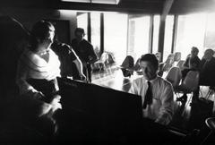 Pat Woodbury, facing right as John Cage plays the piano, facing down, Putah Creek Lodge, Davis California, 1969