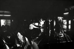 John Cage seated at piano with Pat Woodbury standing next to him, backs to camera, Putah Creek Lodge, Davis California, 1969