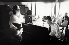 Pat Woodbury singing, facing right as John Cage plays the piano, facing down, Putah Creek Lodge, Davis California, 1969