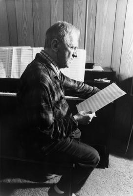 Leo Ornstein, seated at piano, leaning slightly forward, facing right, looking at a musical score, Brownsville TX, 1981