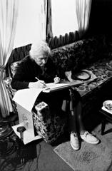 Pauline Ornstein seated on a couch examining a document, Brownsville TX, 1981