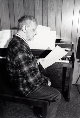 Leo Ornstein, seated at piano, facing right, looking at a musical score, Brownsville TX, 1981